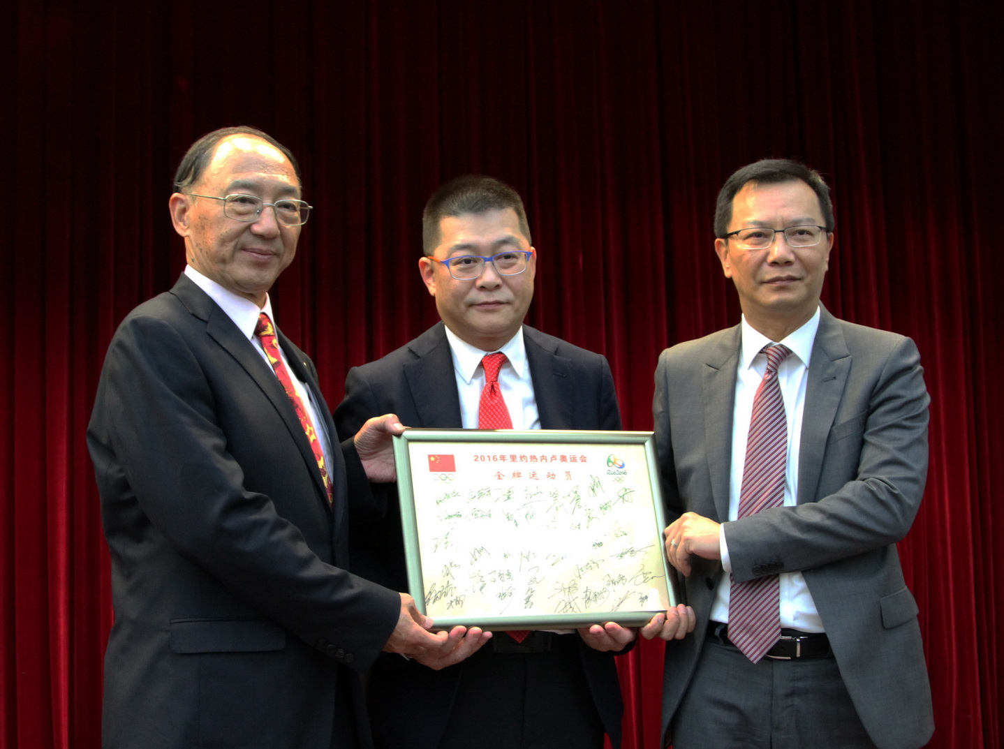 刘鹏(左一)向曾宪梓博士致送全体里约奥运中国金牌运动员的签名簿